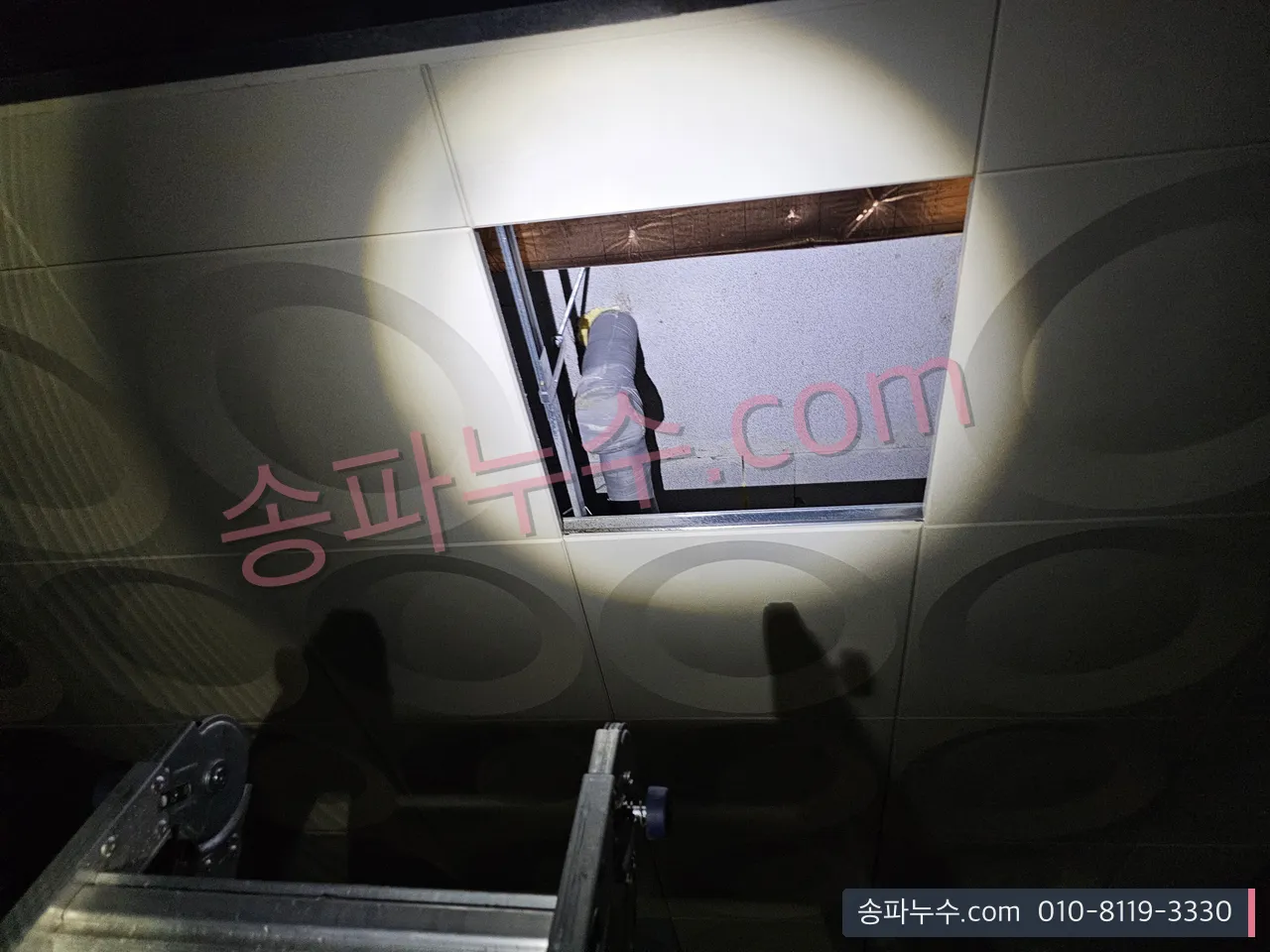 조명을 비춰 천장 점검구 안쪽 배관을 확인하는 장면