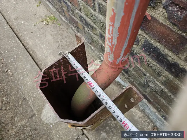 빗물 선홈통 하단 절단부에 줄자를 댄 근접
